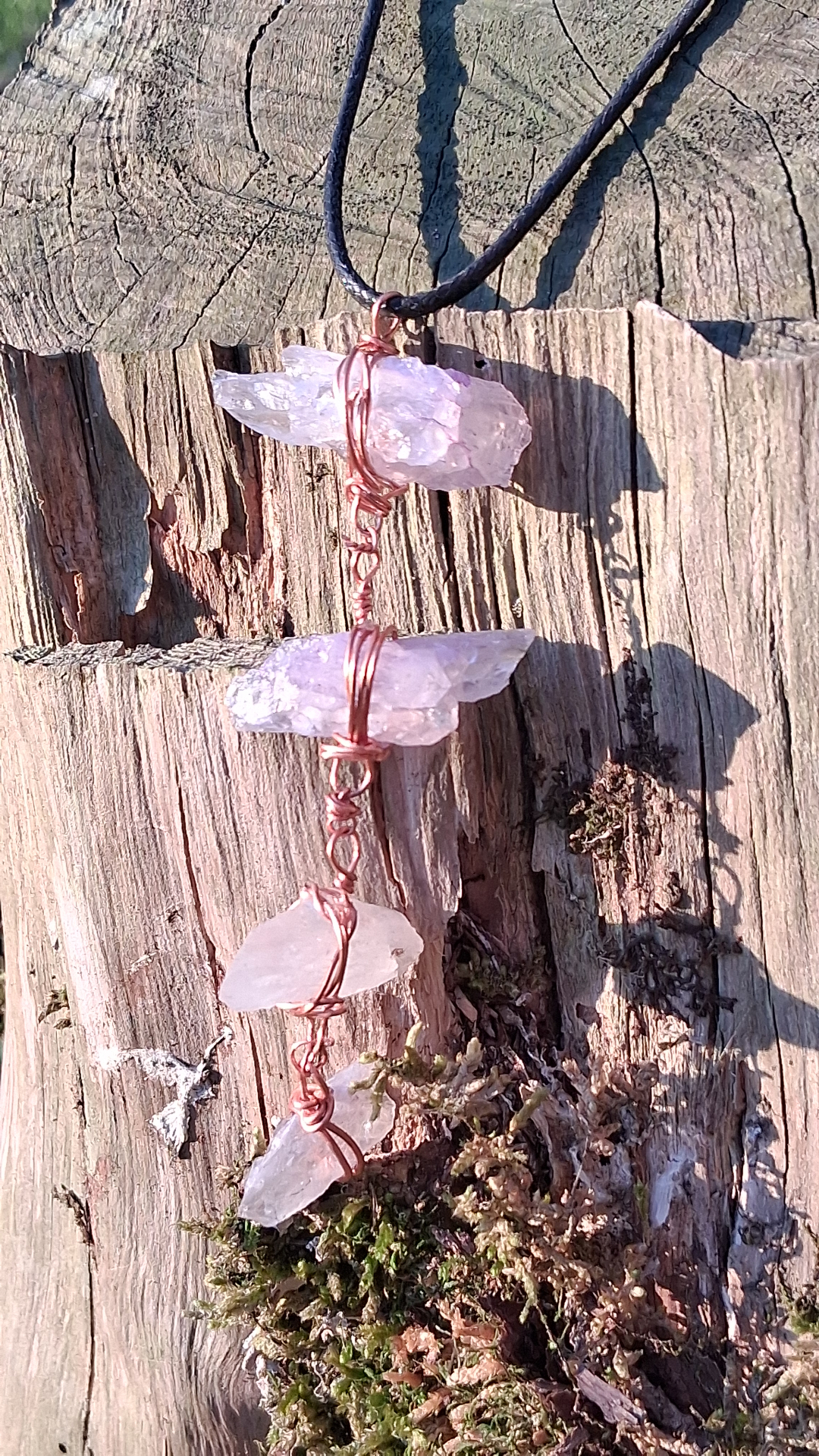 A wand of rose quartz, hand-wrapped in copper, resting on a weathered stump